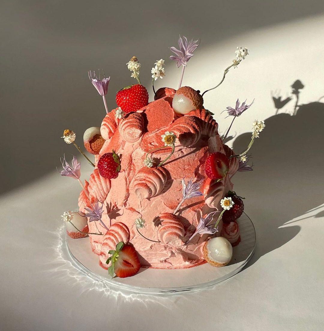 Rosafarbene Torte mit Früchten und Blumen, symbolisiert die Verlockung von zuckerreichen Lebensmitteln und die Problematik des Zuckerkonsums.