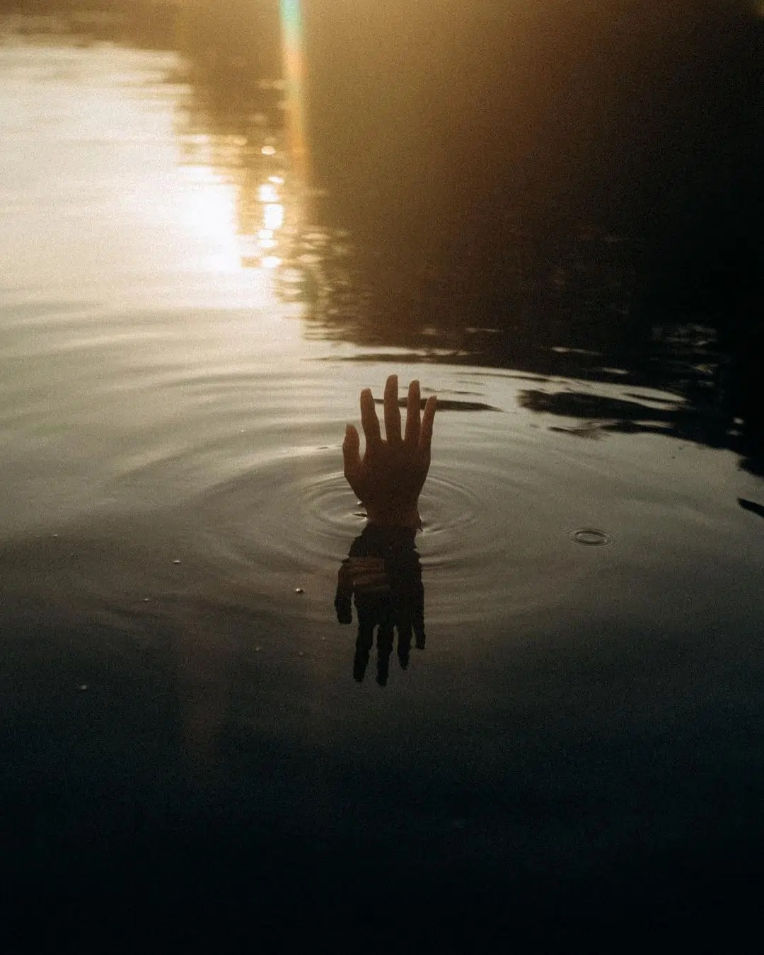 Hand im Wasser bei Sonnenuntergang. So wie das Wasser beruhigt, hilft Küssen, Stress abzubauen und inneren Frieden zu finden.
