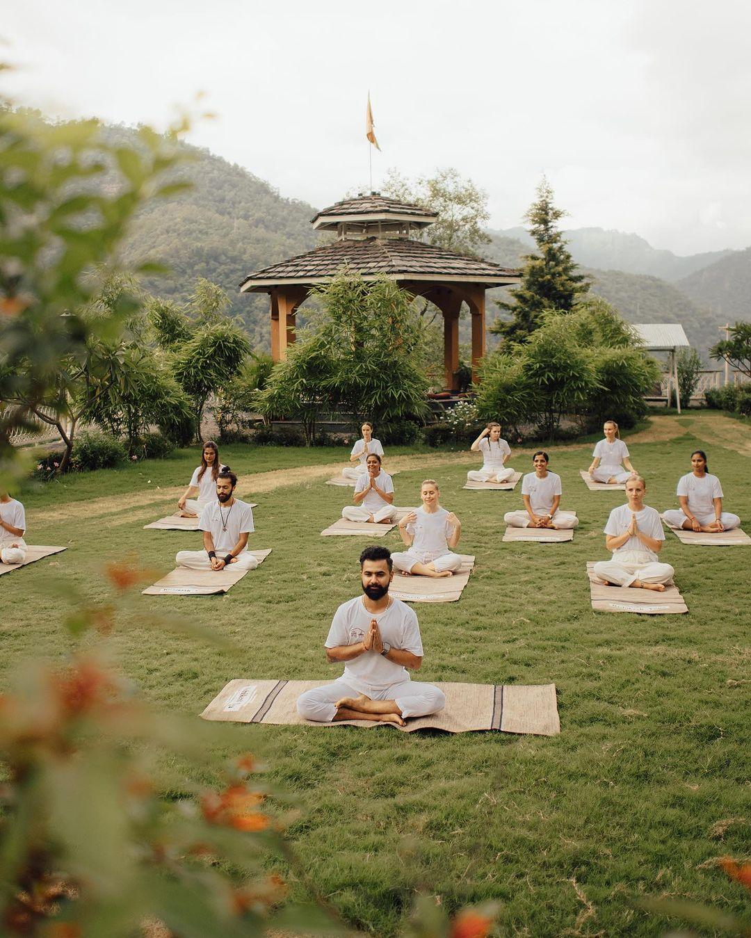 Eine Yoga-Gruppe sitzt meditierend in einer Gartenlandschaft, führt Atemübungen durch – Mantren und Meditation helfen, das Leben zu verbessern.