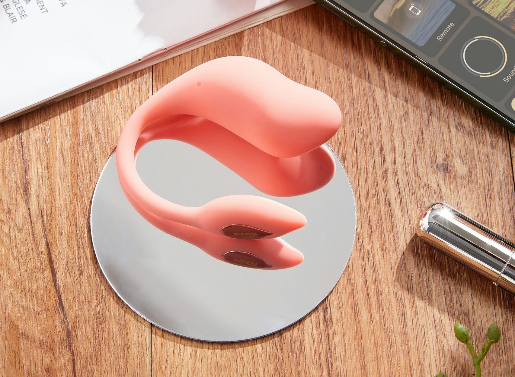 Smart Vibrator in pinker Farbe mit moderner Smartphone-App-Steuerung auf einem Spiegel, dekoriert mit Blumen und Magazin