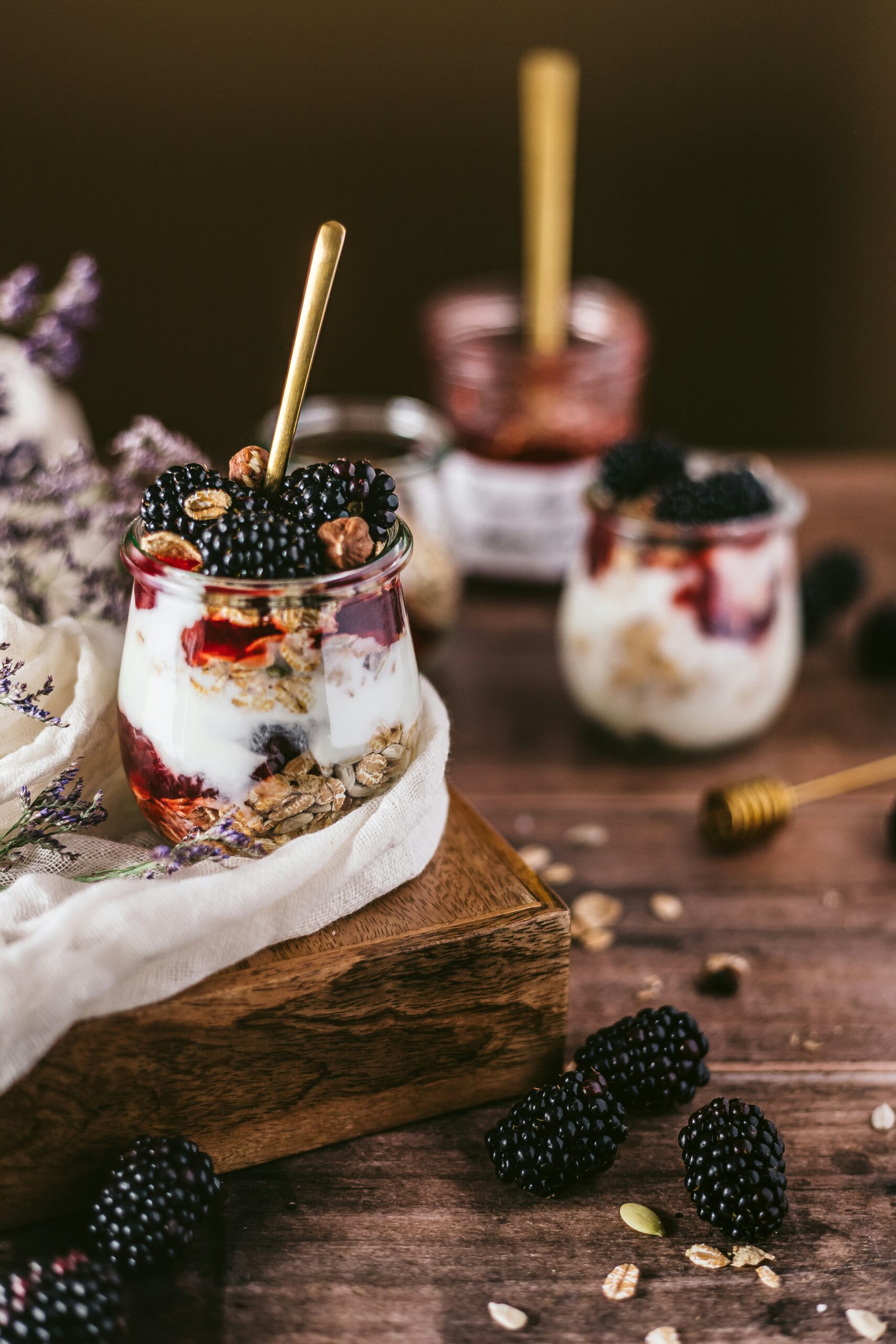 Ein Glas mit Schichten aus Joghurt, Müsli und frischen Brombeeren, garniert mit einem goldenen Löffel
